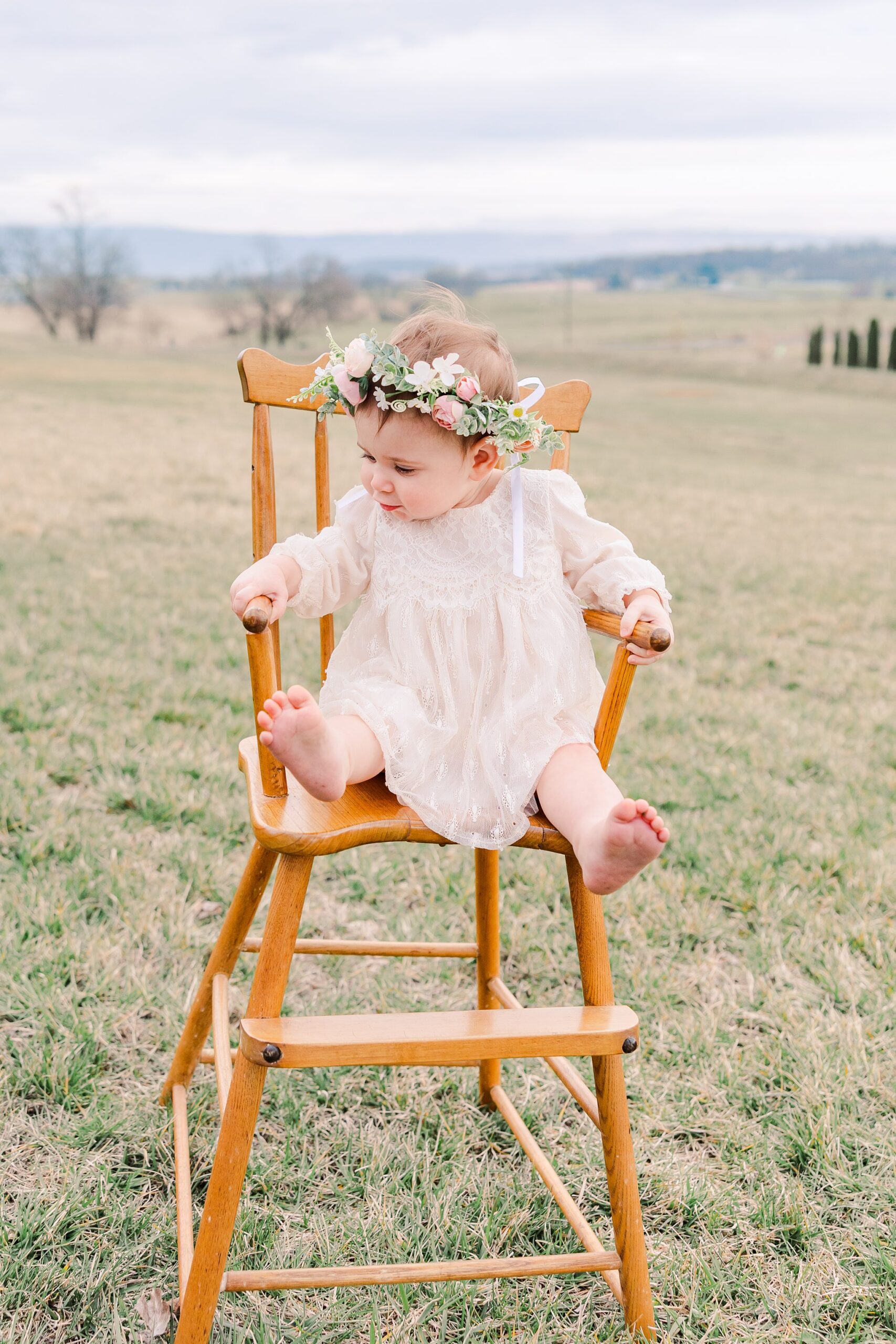 one year old little girl sitting in antique wooden high chair outside