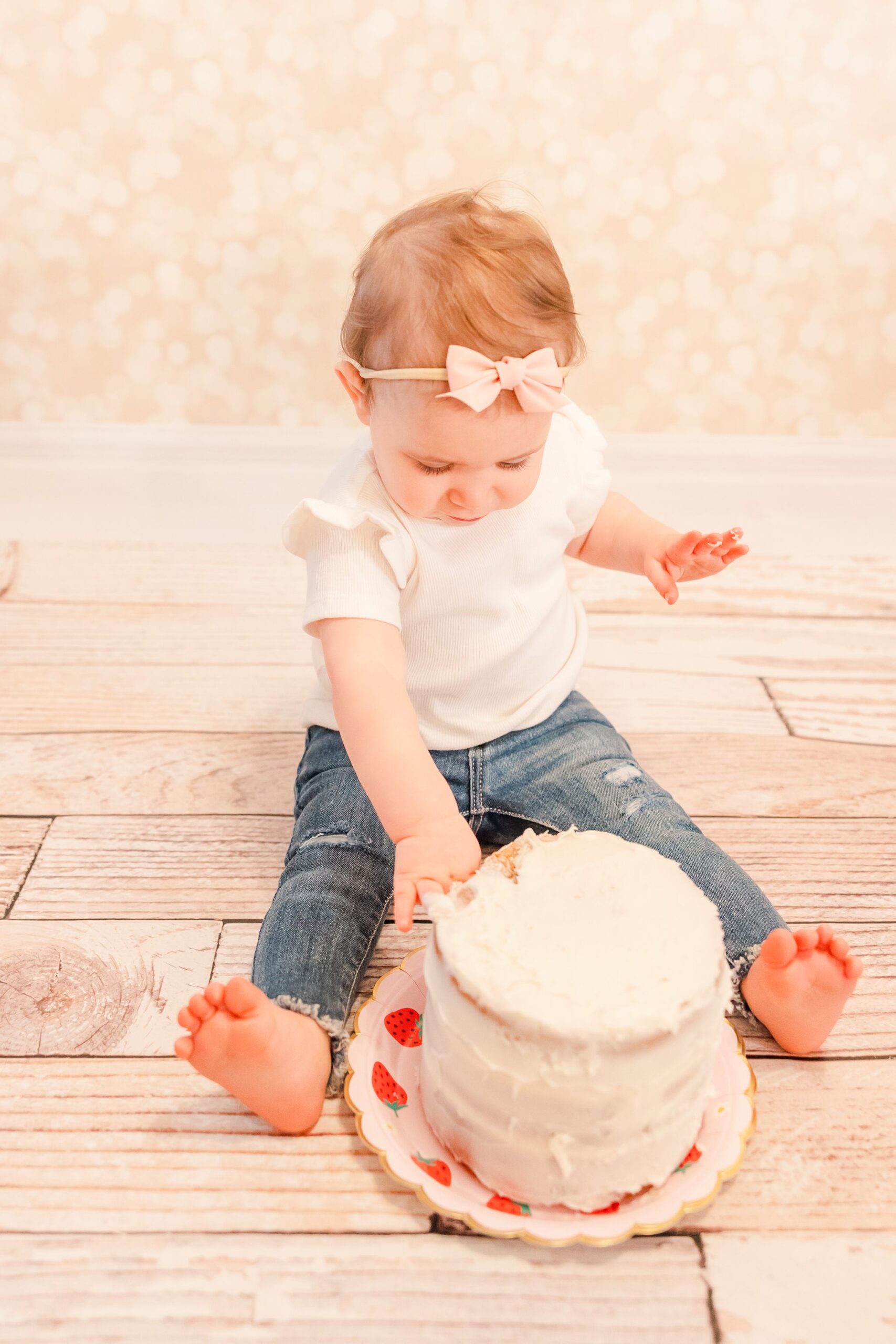 one year old in jeans smashing a white birthday cake