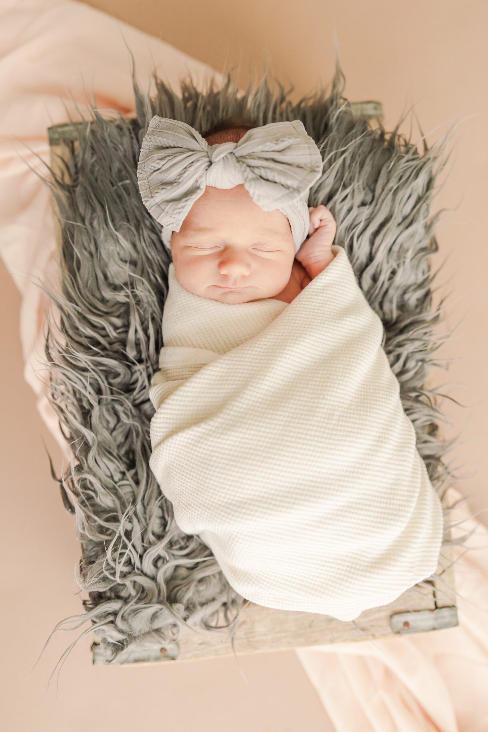 newborn girl swaddled in white with grey fur and headband