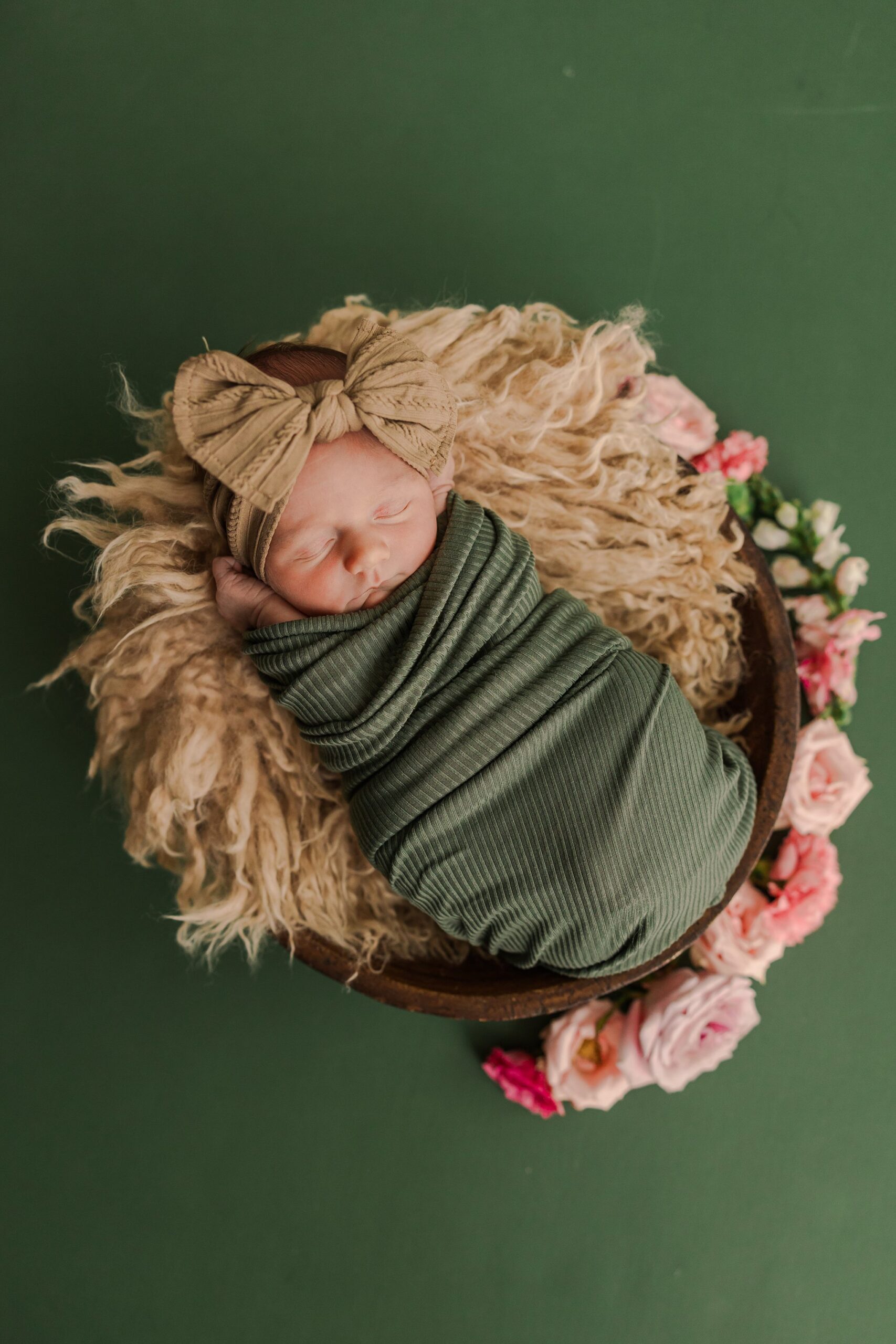 baby swaddled in a bowl with pink fresh flowers around her