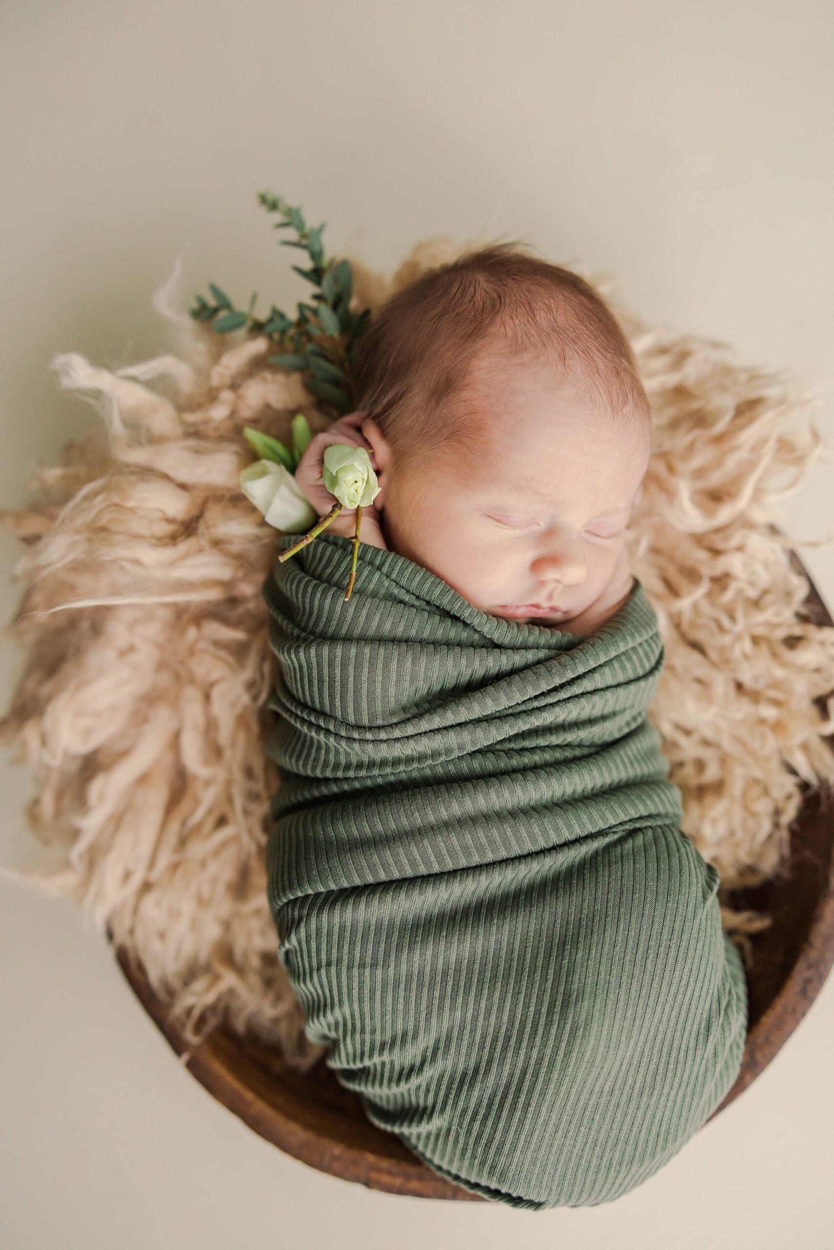 baby swaddled in green wrap with cream fur in bowl