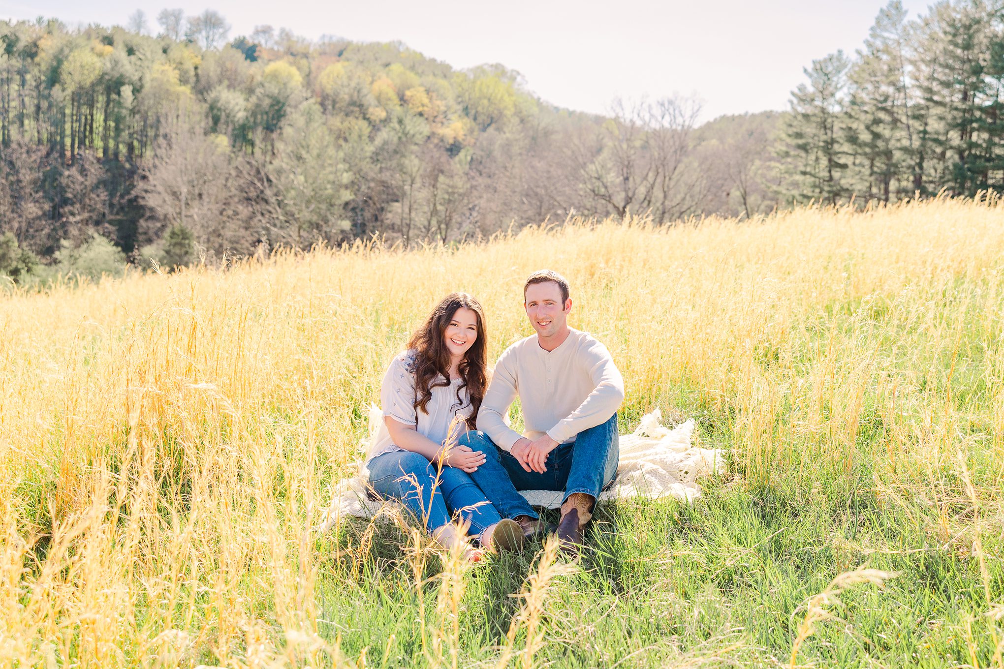 engagement couple sitting together on quilt in tall grass
