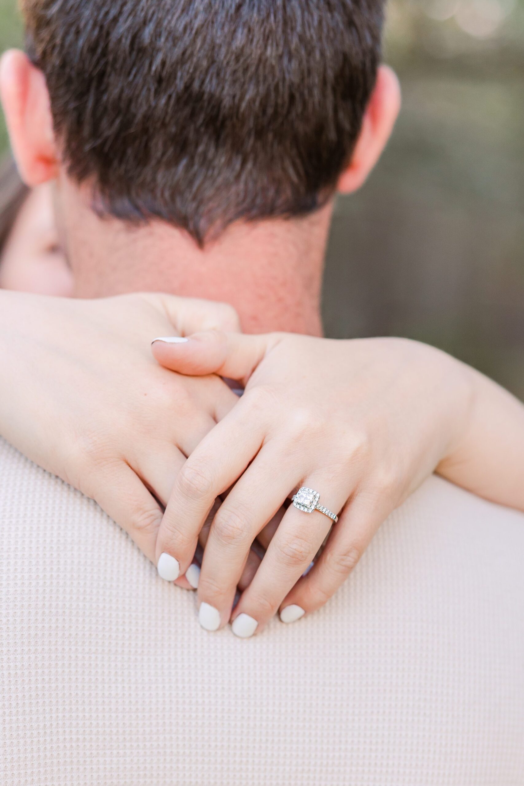 woman hands wrapped around guys neck showing off engagement ring