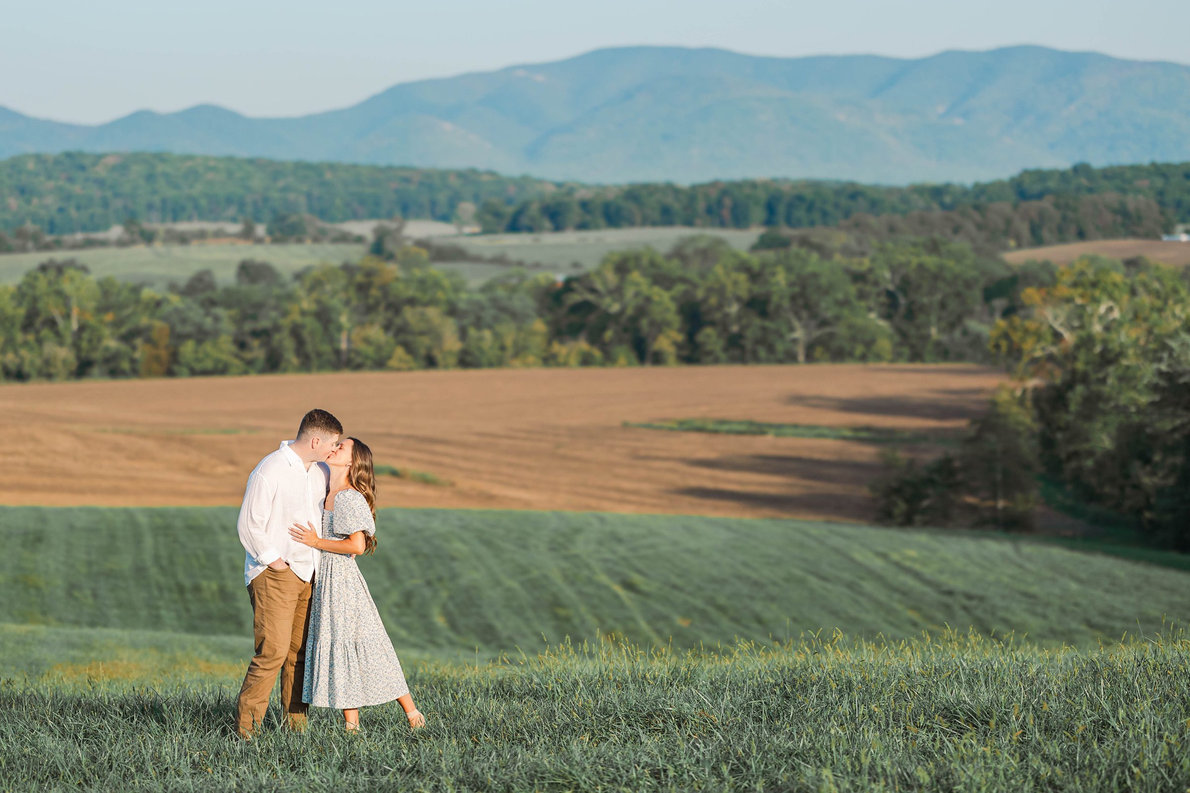 young couple kissing in a field in front of mountains