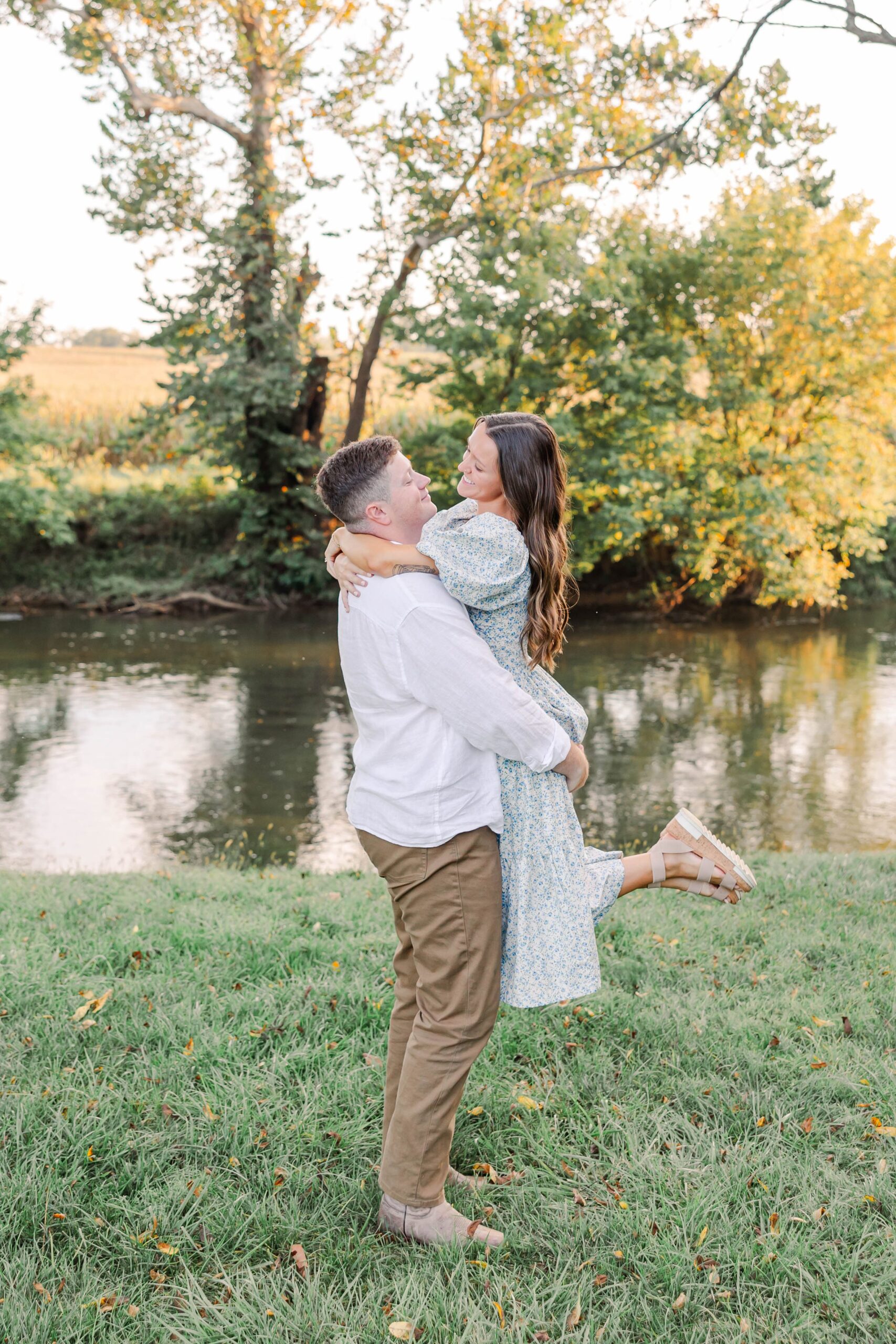 engaged couple with man picking up woman in front of a river