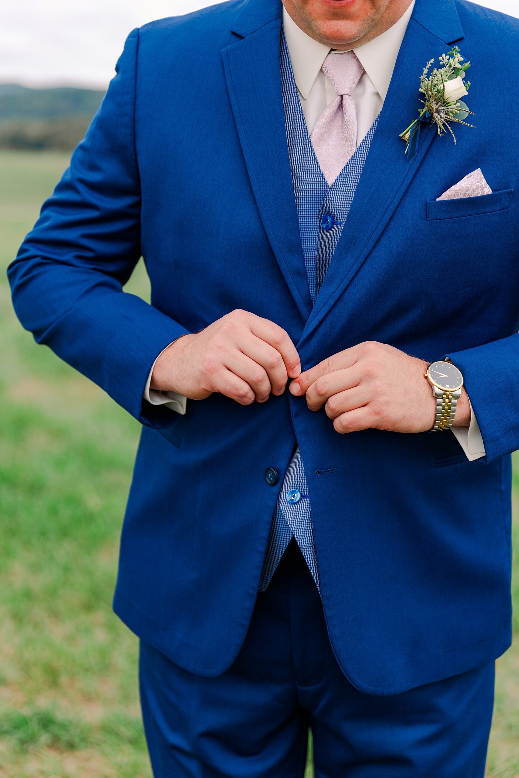 man buttoning a blue suit with gold watch and pink tie
