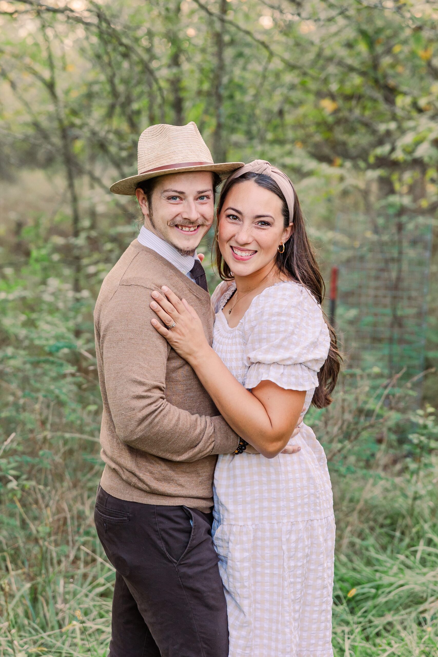 A young couple embrace and smile at the camera in a field of grass. 